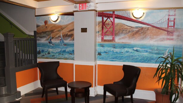 A lobby with a mural of the Golden Gate Bridge, two black chairs, a small table, and a potted plant. - Layne Hotel (San Francisco)