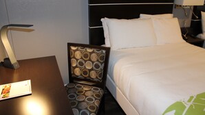 A hotel room with a bed, a nightstand with a lamp, and a chair with a patterned backrest. - Layne Hotel (San Francisco)