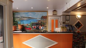 A reception area with a mural of a coastal scene, a clock on the wall, and a book display. - Layne Hotel (San Francisco)