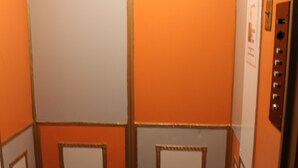 An elevator interior with orange walls, a patterned carpet, and a control panel on the right. - Layne Hotel (San Francisco)