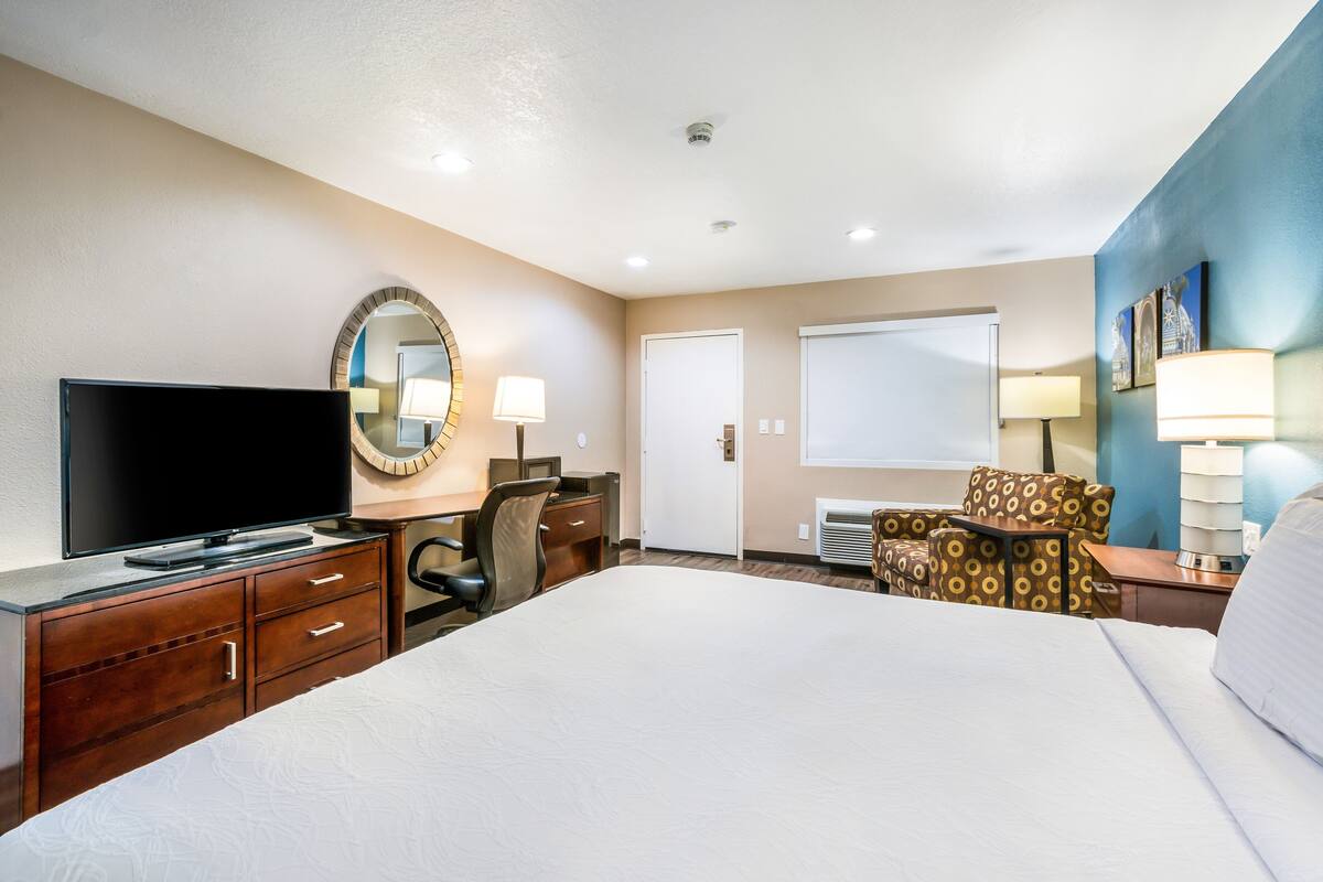 A hotel room with a bed, a desk with a television, a chair, a lamp, and a large mirror.