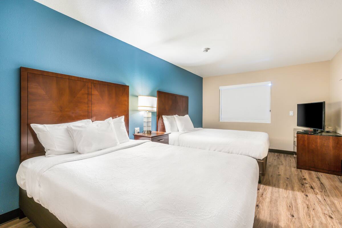 A hotel room with two beds, a TV, and a desk.