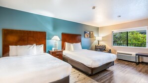 Habitación de hotel con dos camas, cabecero de madera, lámparas de noche, mesitas de noche y ventana con vistas a zonas verdes.