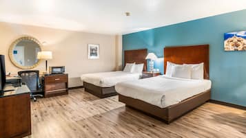 Habitación de hotel con dos camas, un escritorio, una silla, una lámpara de escritorio, un espejo y un cuadro en la pared.