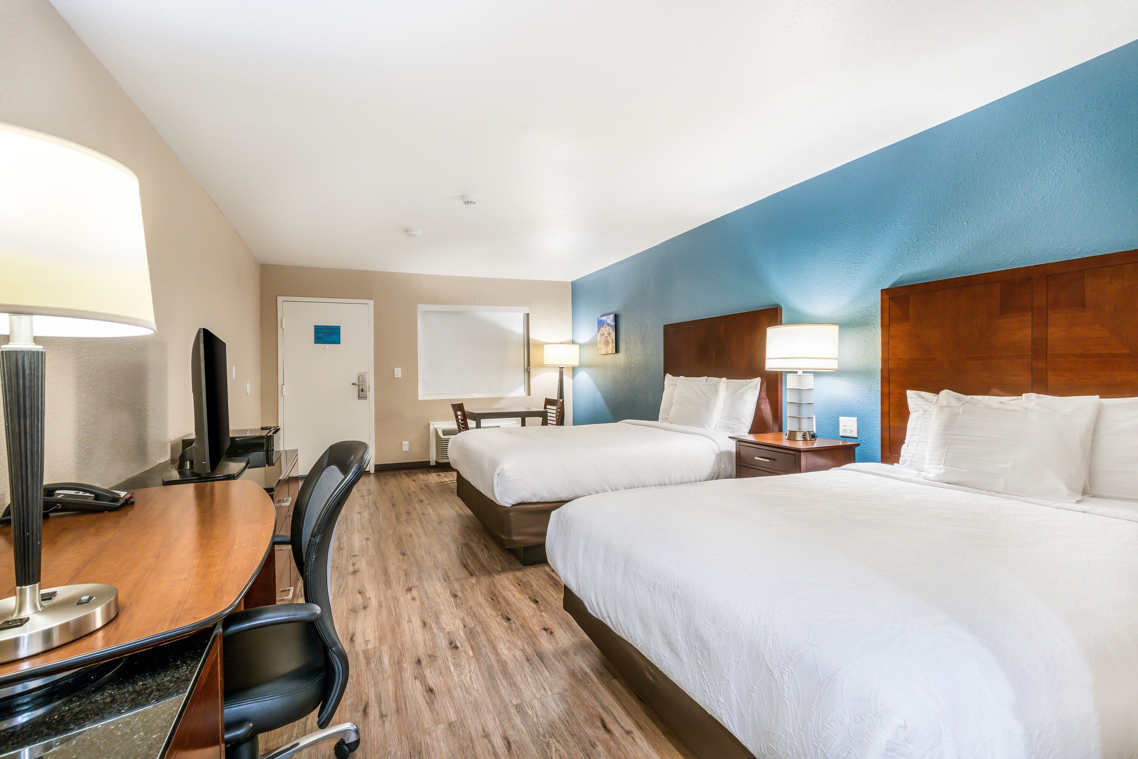 Una habitación de hotel con dos camas, un escritorio con silla, un televisor y una lámpara.