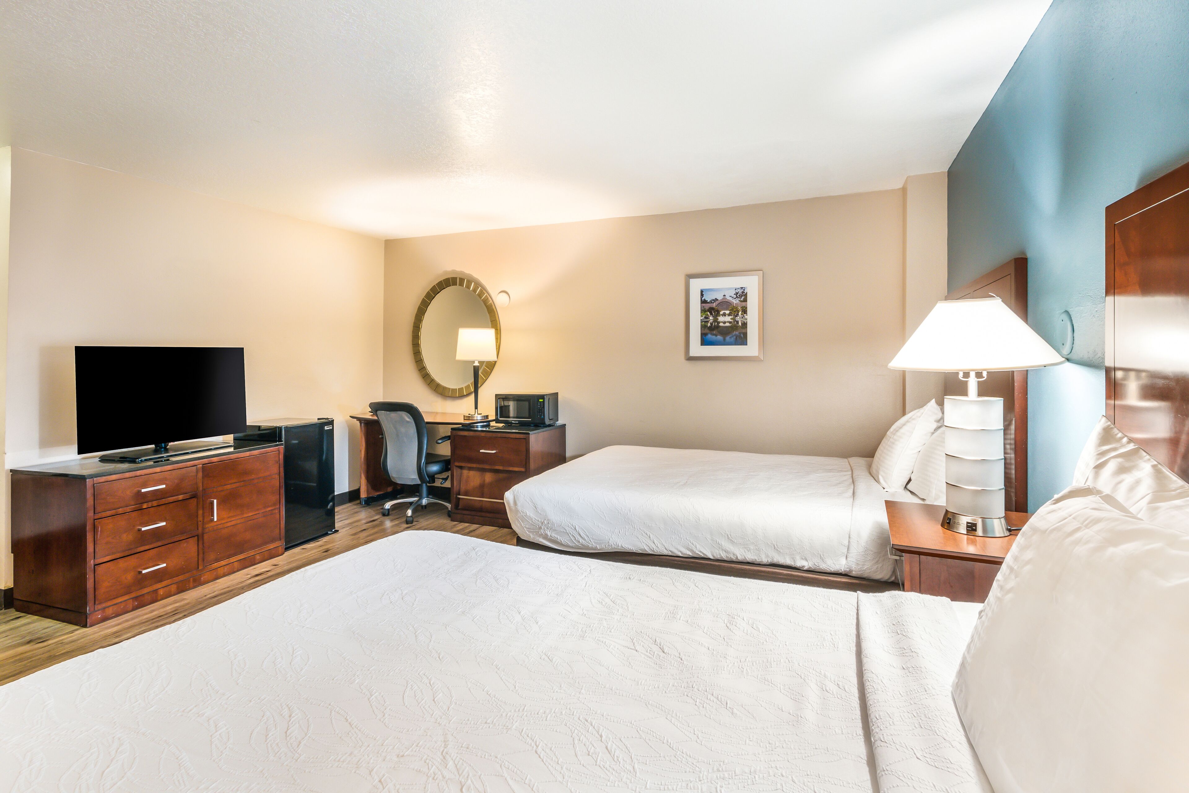 A hotel room with two beds, a desk with a flat-screen TV, a coffee maker, and a desk lamp.