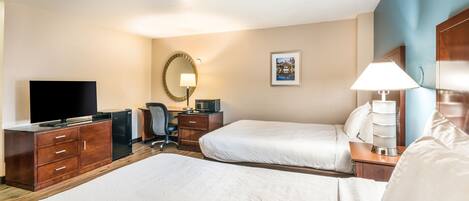 A hotel room with two beds, a desk with a flat-screen TV, a coffee maker, and a desk lamp.