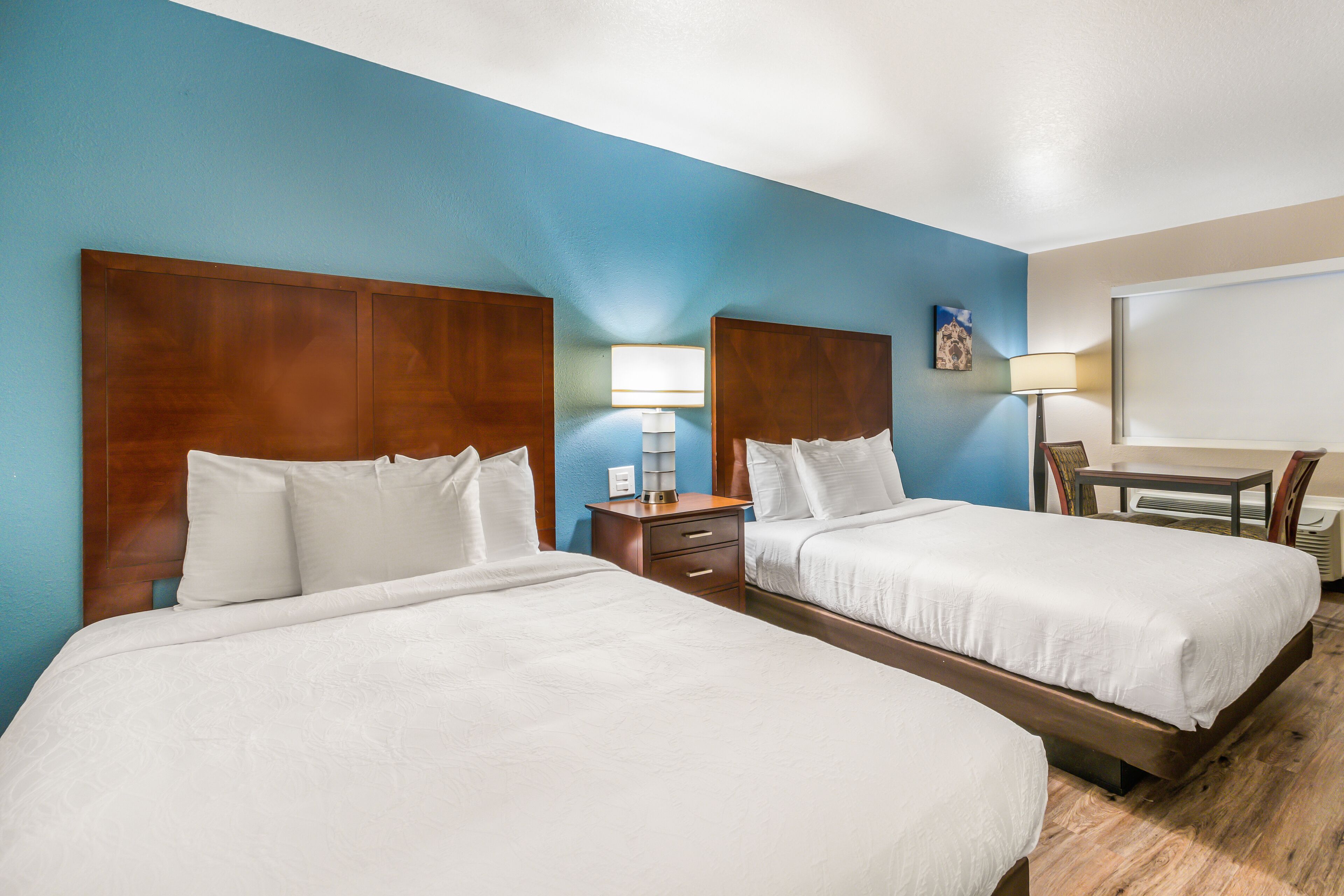 A hotel room with two beds, a desk, and a chair.