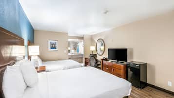 Habitación de hotel con dos camas, un escritorio con computadora, televisor y refrigerador.