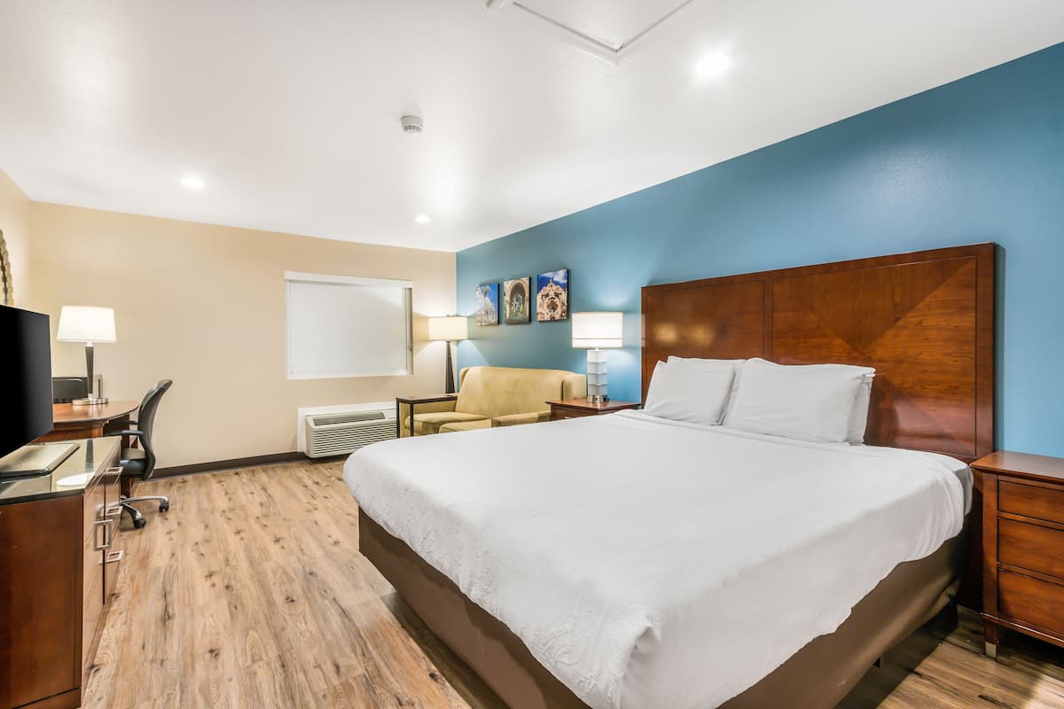 A hotel room with a large bed, a desk with a chair, a TV, and a lamp.