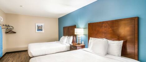 A hotel room with two beds, wooden headboards, a nightstand with a lamp, and a framed picture on the wall.