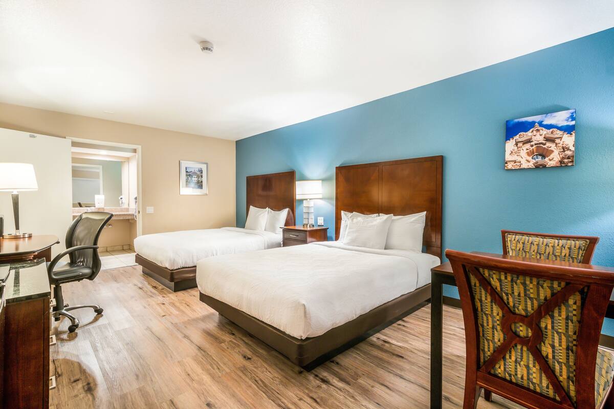 A hotel room with two beds, a desk, a chair, and a nightstand.