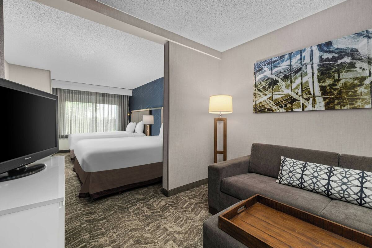 A hotel room with a bed, a sofa, a TV, a lamp, and a painting on the wall.