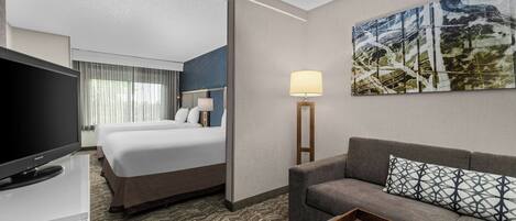 Una habitación de hotel con cama, sofá, televisión, lámpara y un cuadro en la pared.