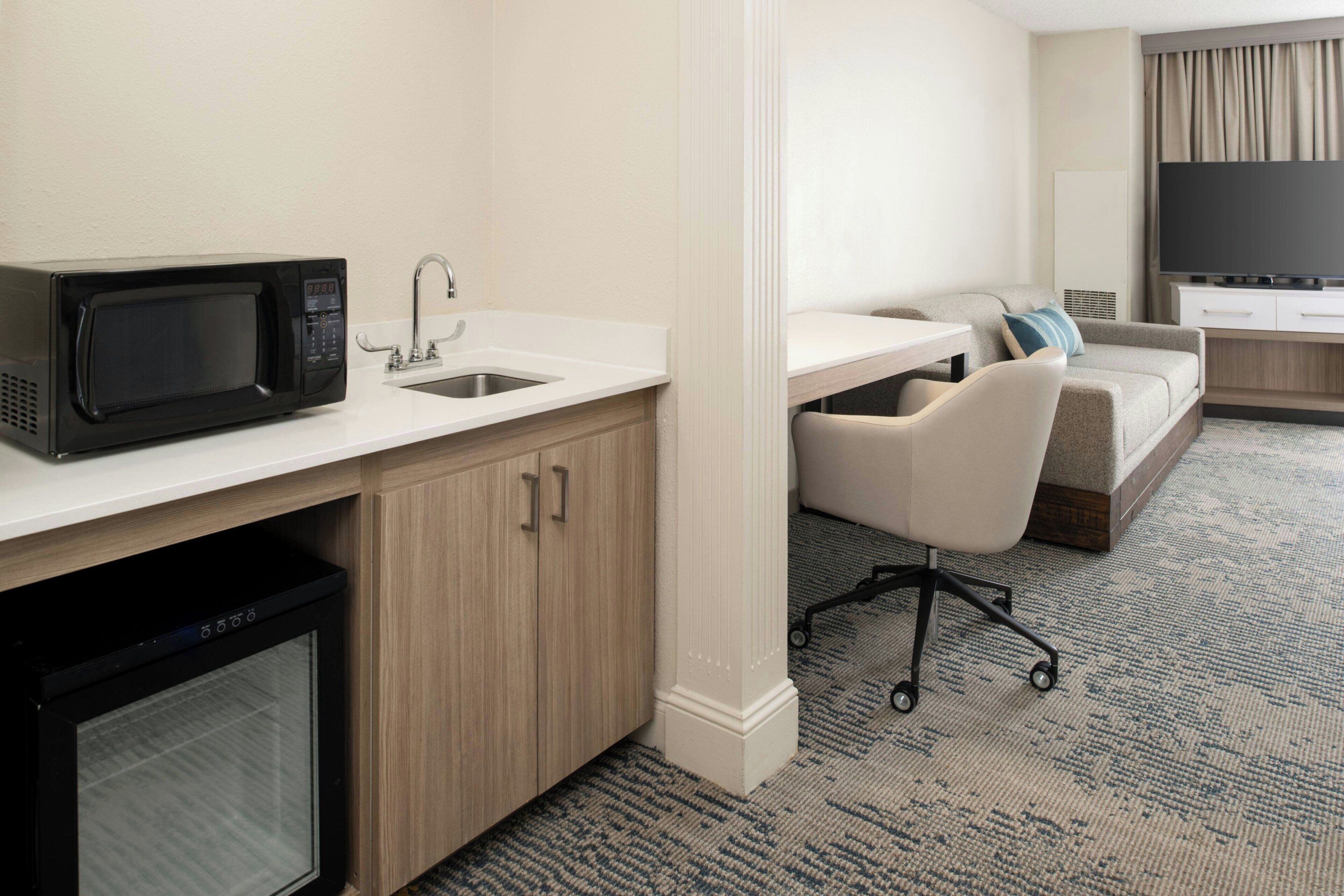 Een compacte hotelkamer met een kitchenette, een bank, een televisie en een klein bureau.
