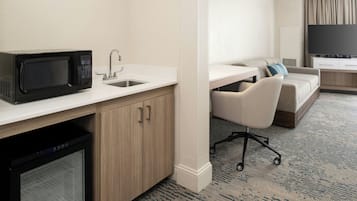 Een compacte hotelkamer met een kitchenette, een bank, een televisie en een klein bureau.