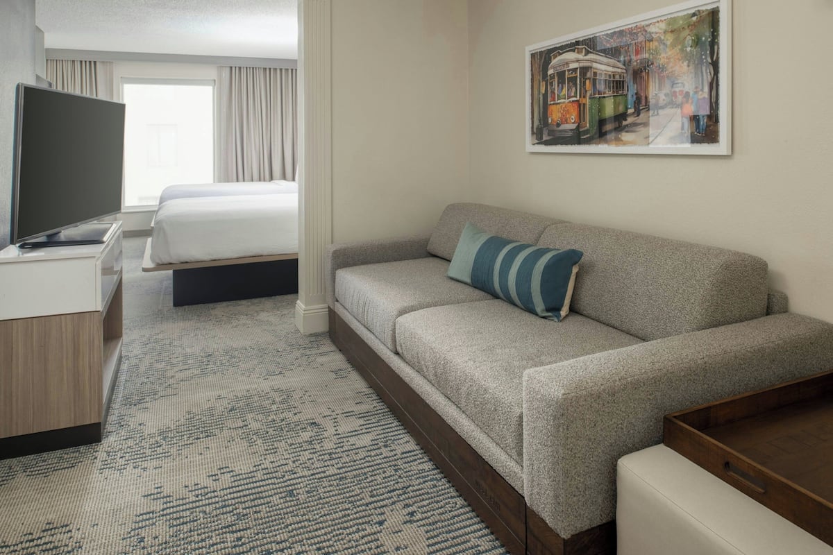 A hotel room with a bed, a sofa, a TV, and a painting on the wall.