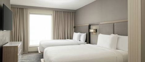 A hotel room with two beds, a flat-screen TV, a desk, and a large window with curtains.