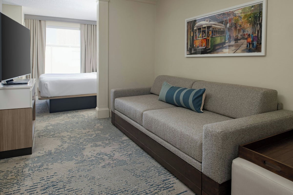 A hotel room with a bed, a sofa, a TV, a painting, and a carpet.