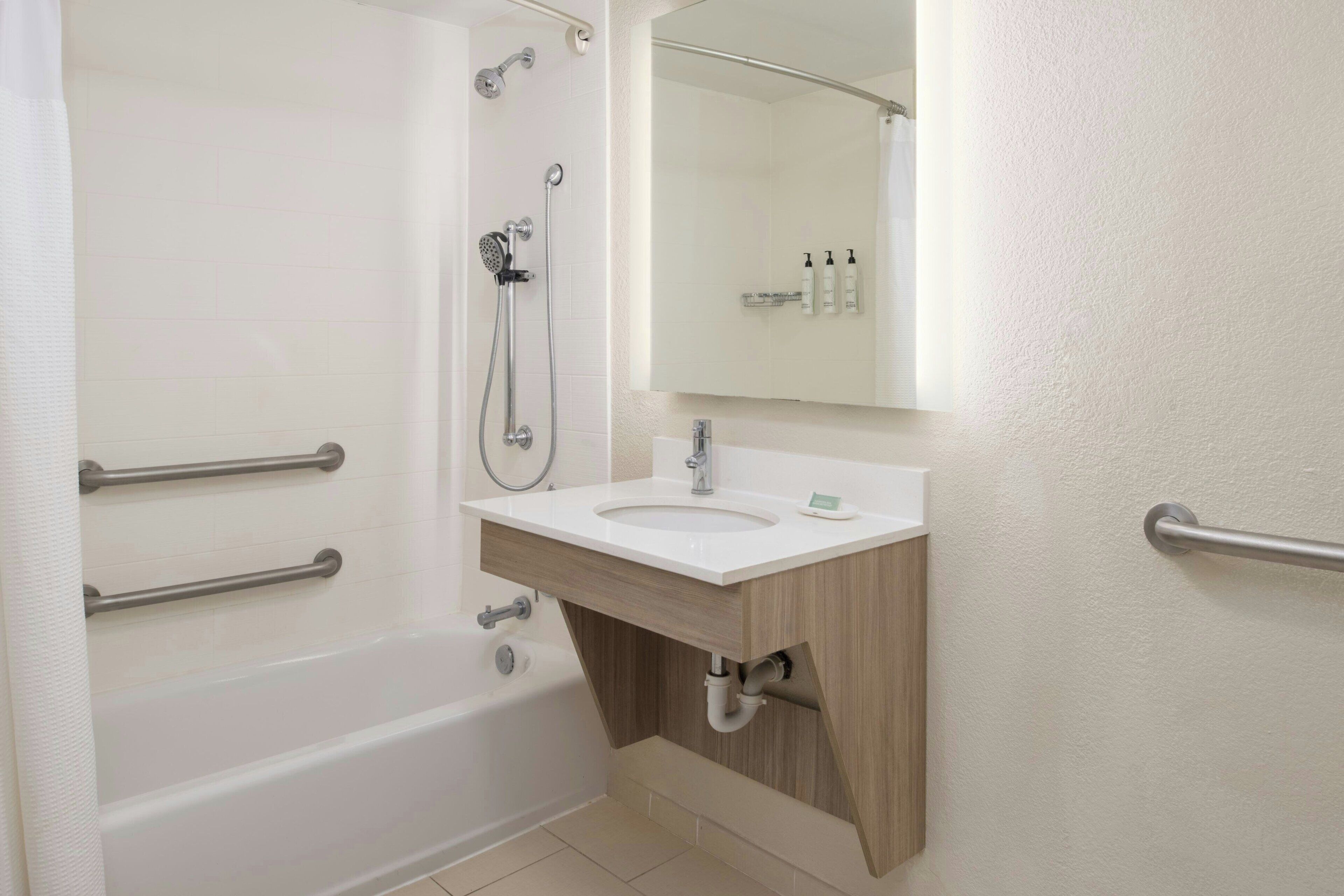 A modern bathroom with a bathtub, a sink with a mirror above it, and a shower with a handheld showerhead.
