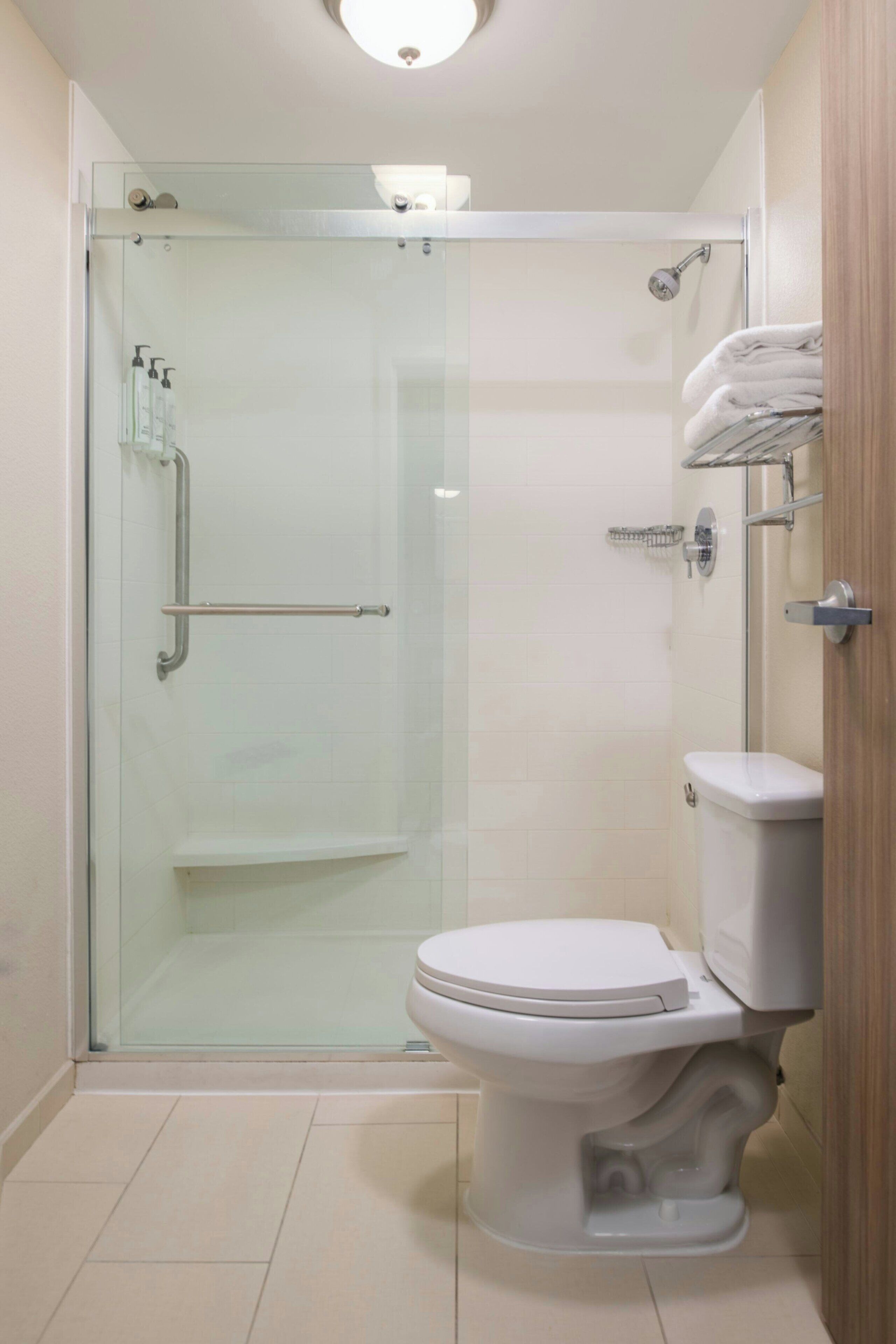 Un baño moderno con ducha de vidrio, inodoro blanco y tocador de madera con toallero.