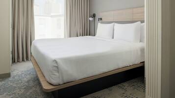 Habitación de hotel con una cama grande, cabecera, mesita de noche, lámpara y vista a edificios a través de la ventana.