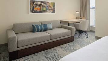 A hotel room with a sofa, a desk, a chair, a bed, and a window with curtains.