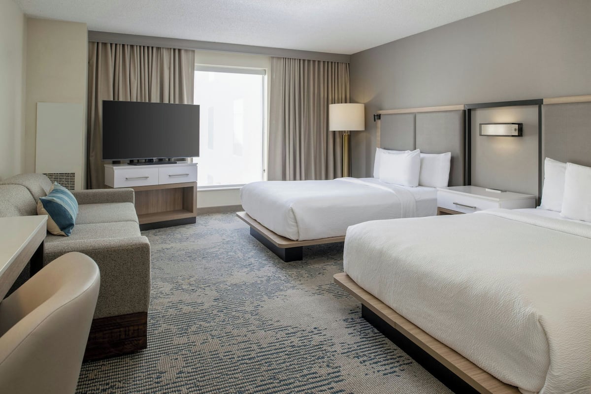 A hotel room with a large bed, a smaller bed, a sofa, a TV, and a desk.