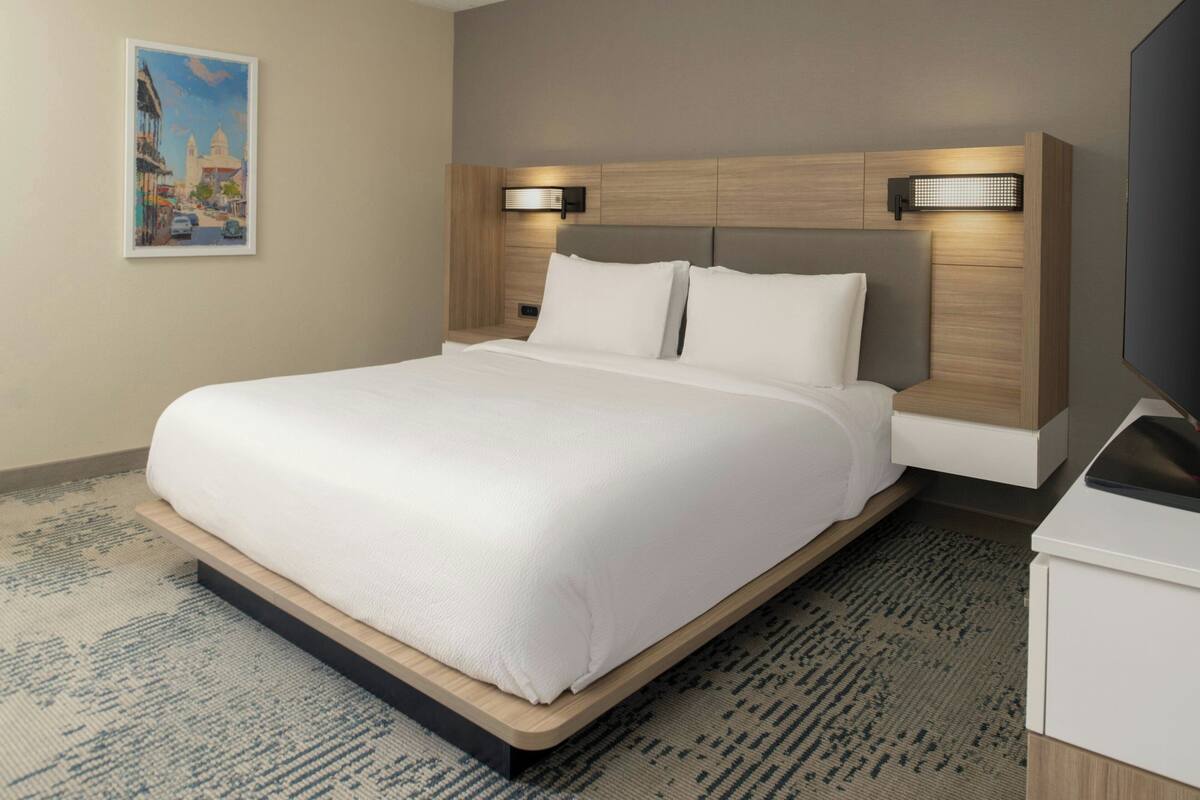 A modern hotel room with a large bed, wooden headboard, and two wall-mounted reading lights.
