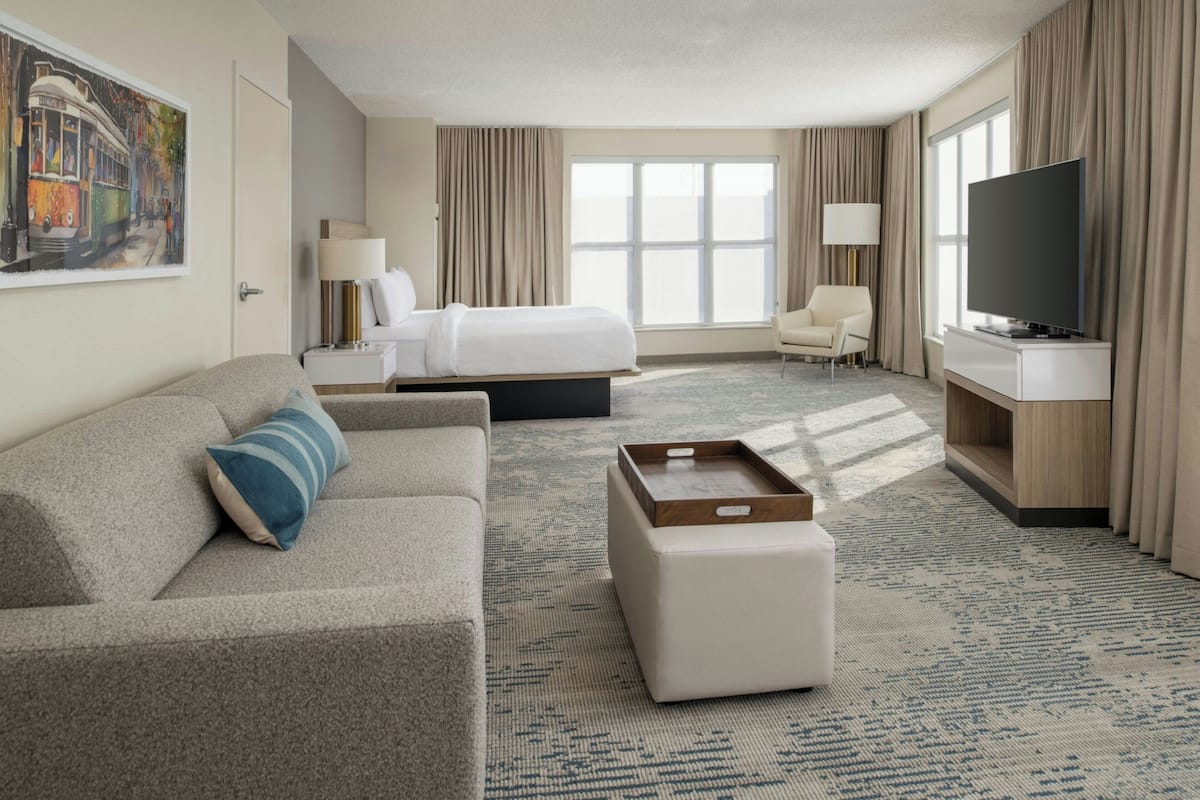 A hotel room with a bed, a sofa, a TV, a desk, and a painting on the wall.