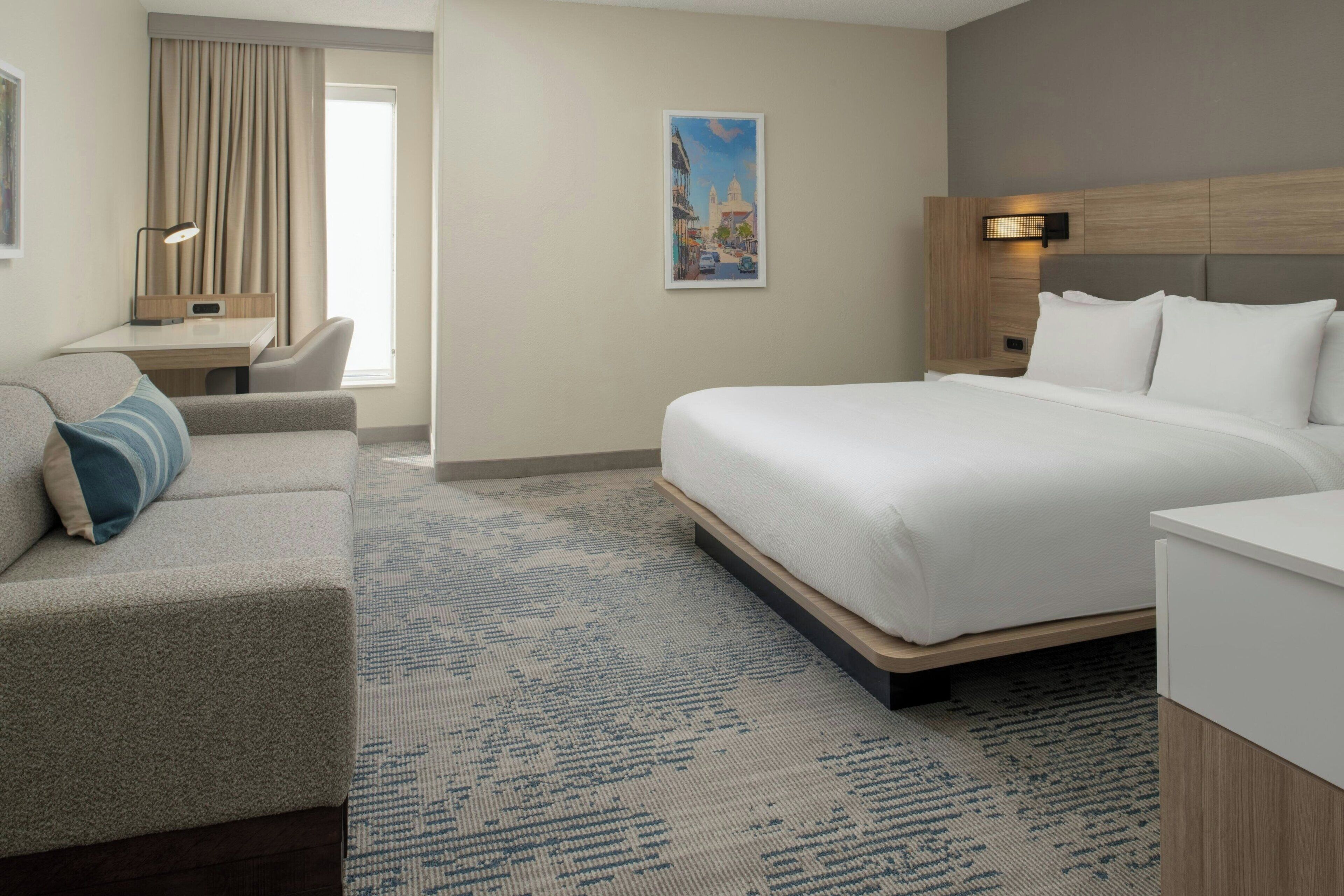A hotel room with a large bed, a desk, a chair, and a window with curtains.