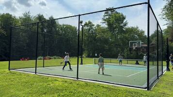 A tennis court enclosed by a netted fence with a basketball hoop in the background.