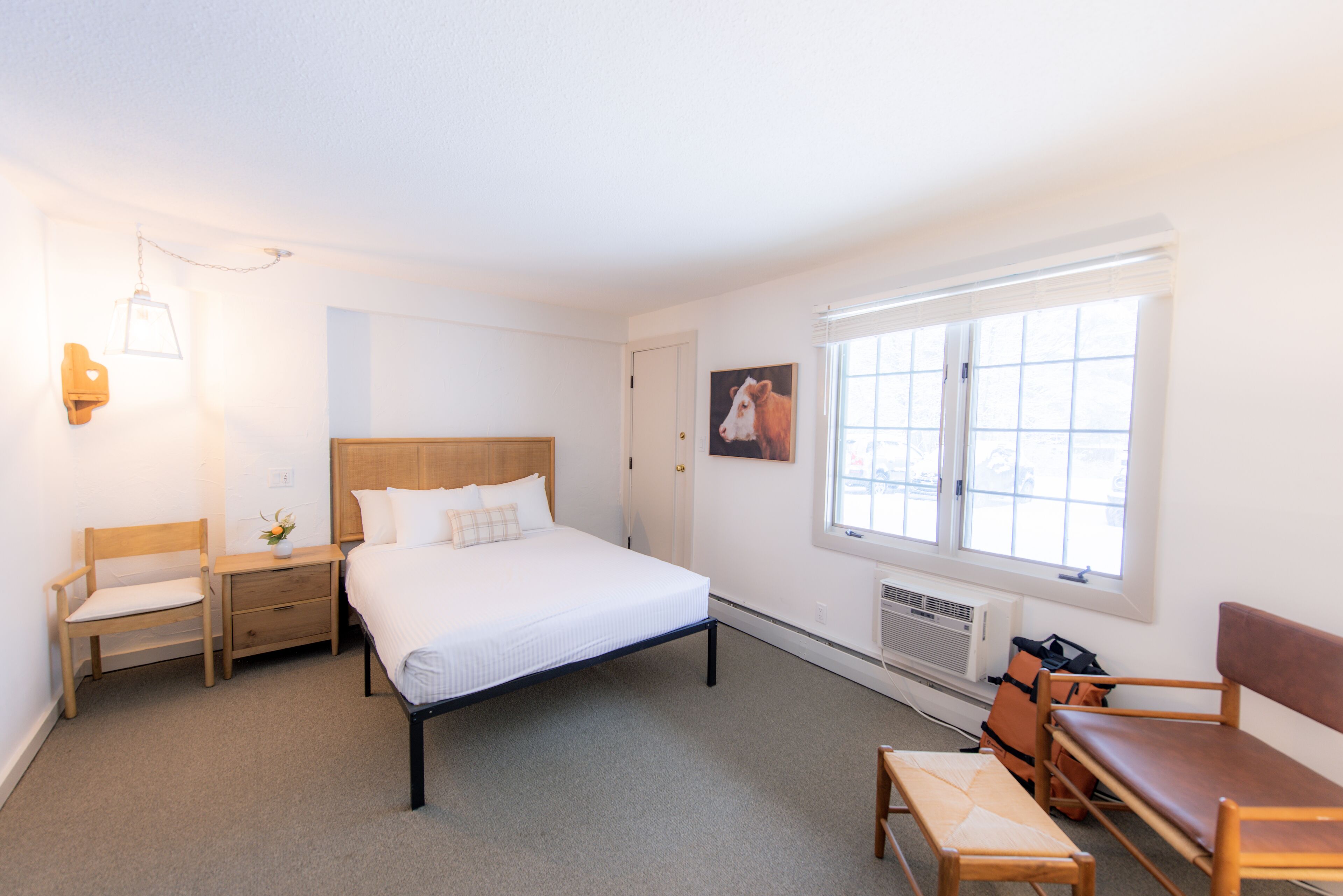 Une chambre à coucher comprenant un lit, des tables de chevet, un banc, une fenêtre et un radiateur.