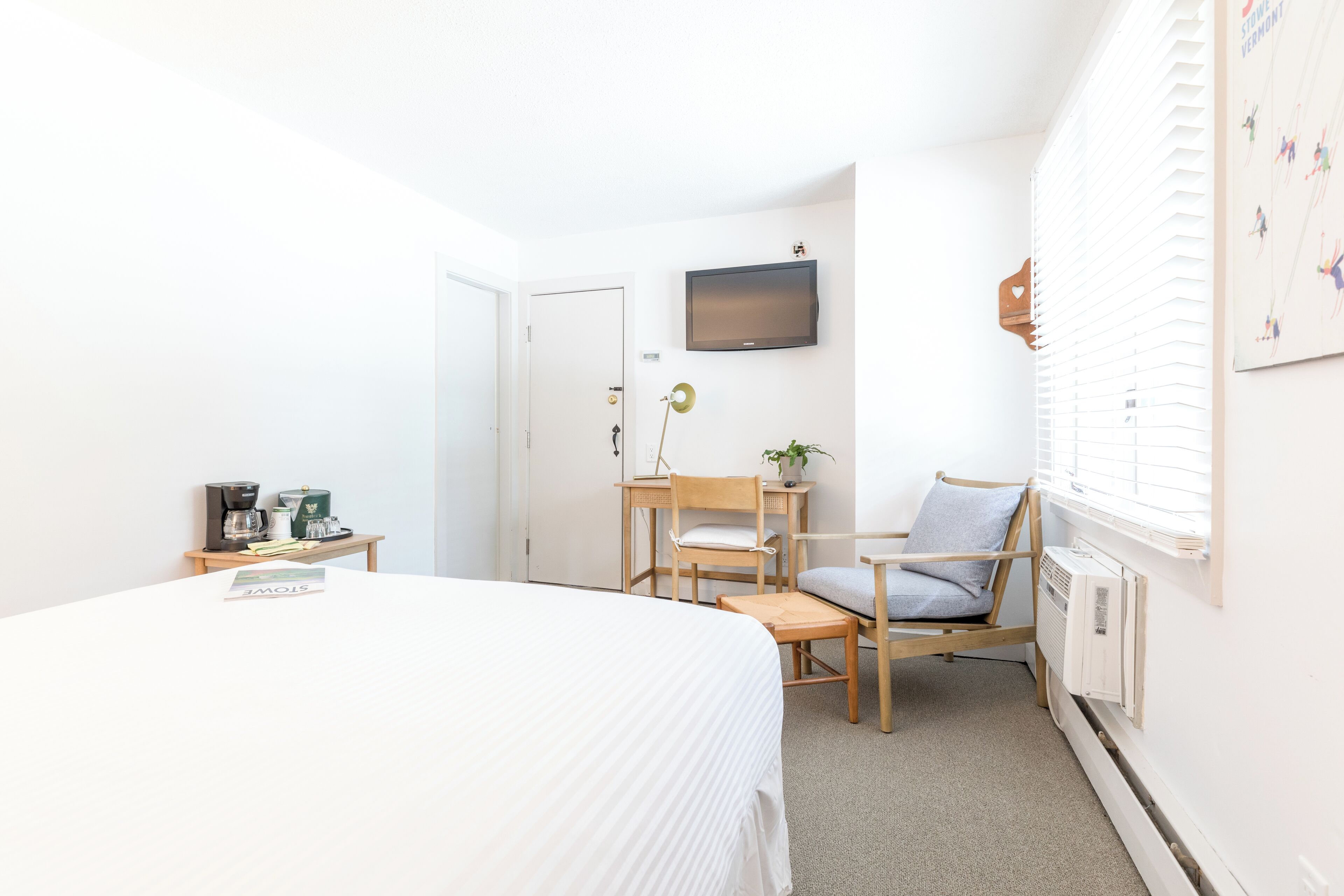 A hotel room with a bed, a desk, a chair, a television, and a window with blinds.