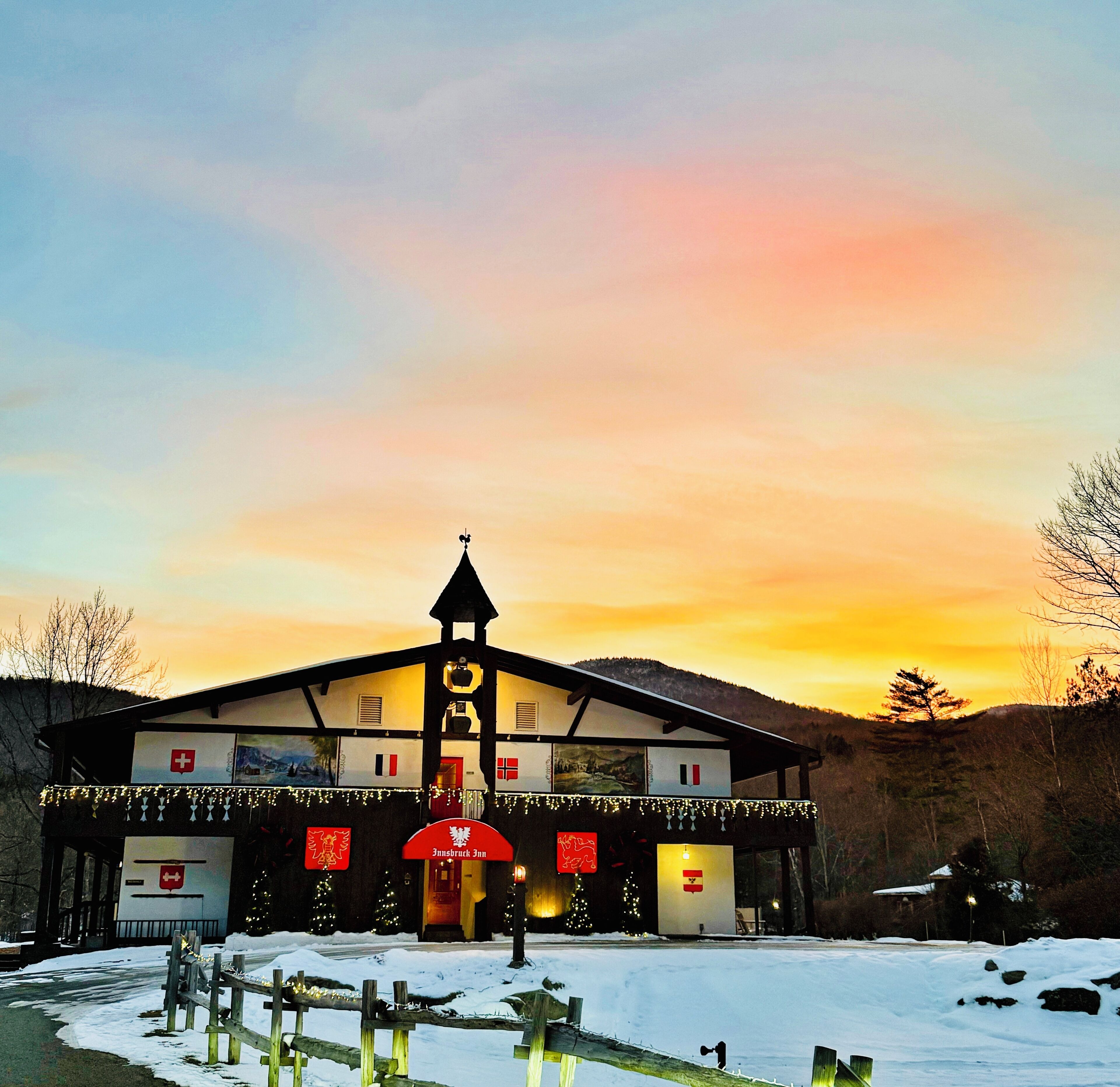 A hotel with a traditional Alpine architectural style, featuring a prominent tower and a signboard with the name "Innbruck Inn".