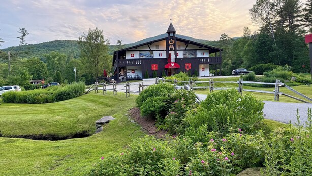 A traditional chalet-style building with a Swiss flag, surrounded by lush greenery and a wooden fence. - Innsbruck Inn at Stowe (Stowe)