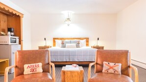 A hotel room with a bed, two armchairs, a wooden coffee table, a microwave, and a kettle on the counter. - Innsbruck Inn at Stowe (Stowe)