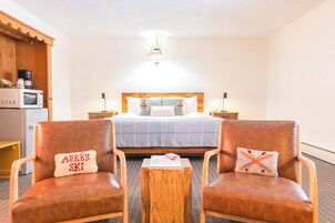 Habitación de hotel con cama, dos sillones, una mesita de centro de madera, microondas y hervidor sobre la encimera.