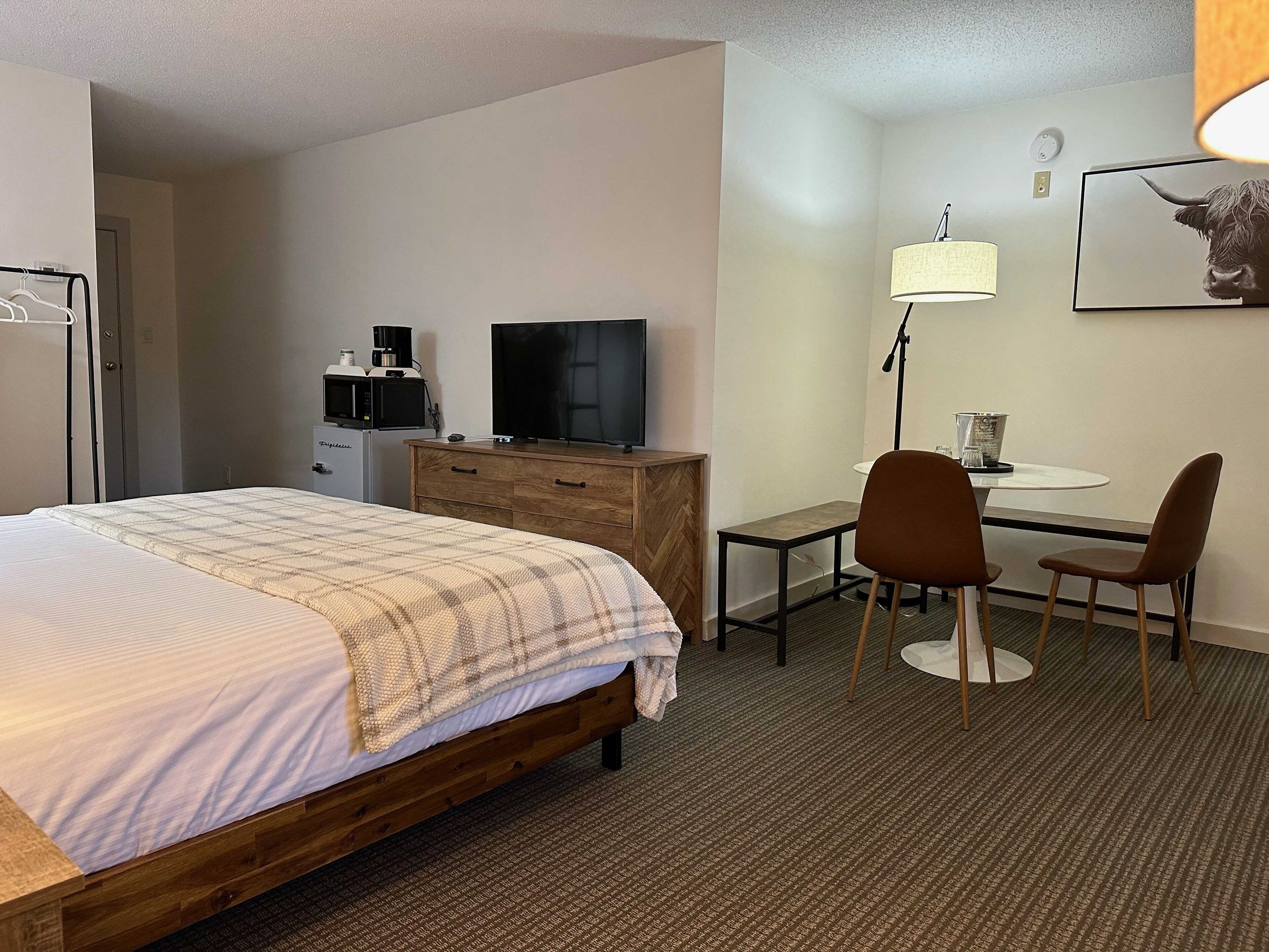 Une chambre d’hôtel équipée d’un lit, d’un bureau, d’une chaise, d’une lampe, d’une télévision et d’un four à micro-ondes.