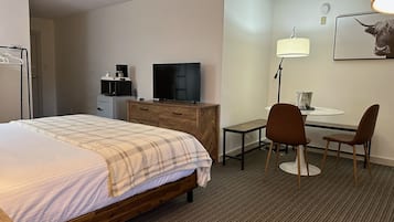 Une chambre d’hôtel équipée d’un lit, d’un bureau, d’une chaise, d’une lampe, d’une télévision et d’un four à micro-ondes.