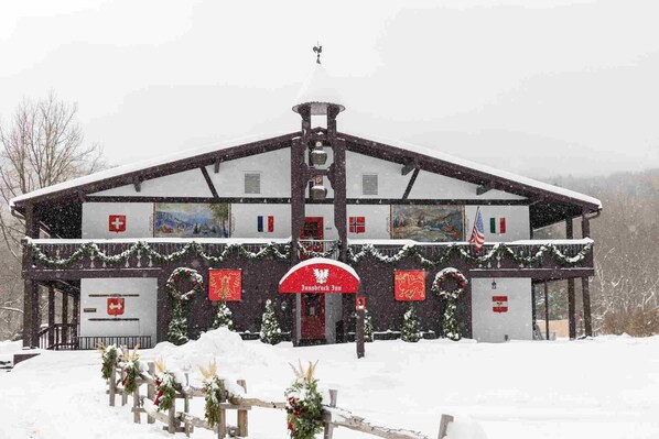 A traditional chalet-style building with a steep roof and a central chimney, surrounded by snow.