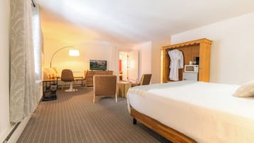 Quarto de hotel com cama, escrivaninha com cadeira, televisão e um armário de madeira com um roupão pendurado.