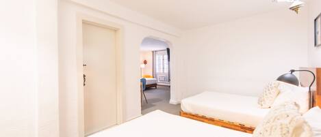 A bedroom with a single bed, a nightstand, and a lamp. There is a door leading to another room.