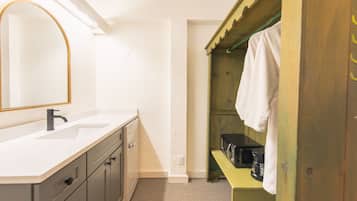 Un baño con un lavamanos blanco, un espejo con marco dorado, una estantería de madera con una toalla, y un microondas negro.