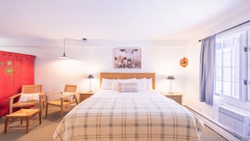 Habitación de hotel con una cama grande, dos mesitas de noche con lámparas, una pared de acento roja y una ventana con cortinas.