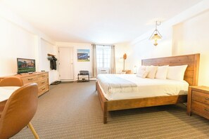 A hotel room with a wooden bed, a desk with a chair, a television, and a painting on the wall.