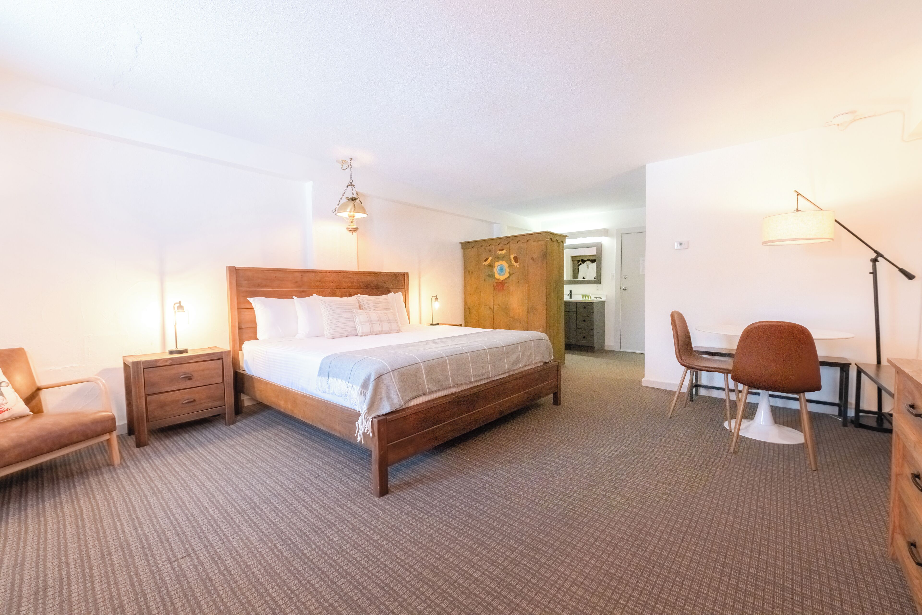 A hotel room with a wooden bed, a desk, a chair, and a wardrobe.