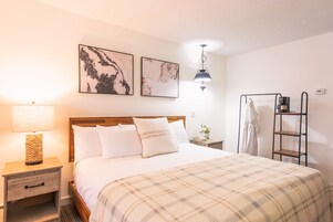 Una cama bien tendida con una manta escocesa, una lámpara de noche y dos cuadros en la pared.