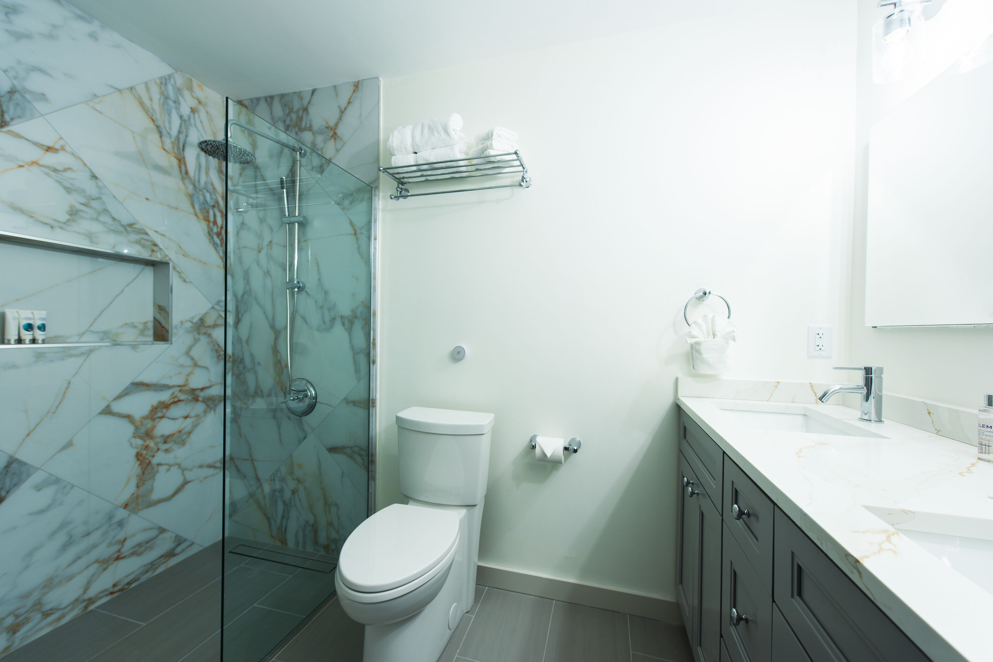 A modern bathroom with a glass shower enclosure, a toilet, a sink, and a vanity with drawers.