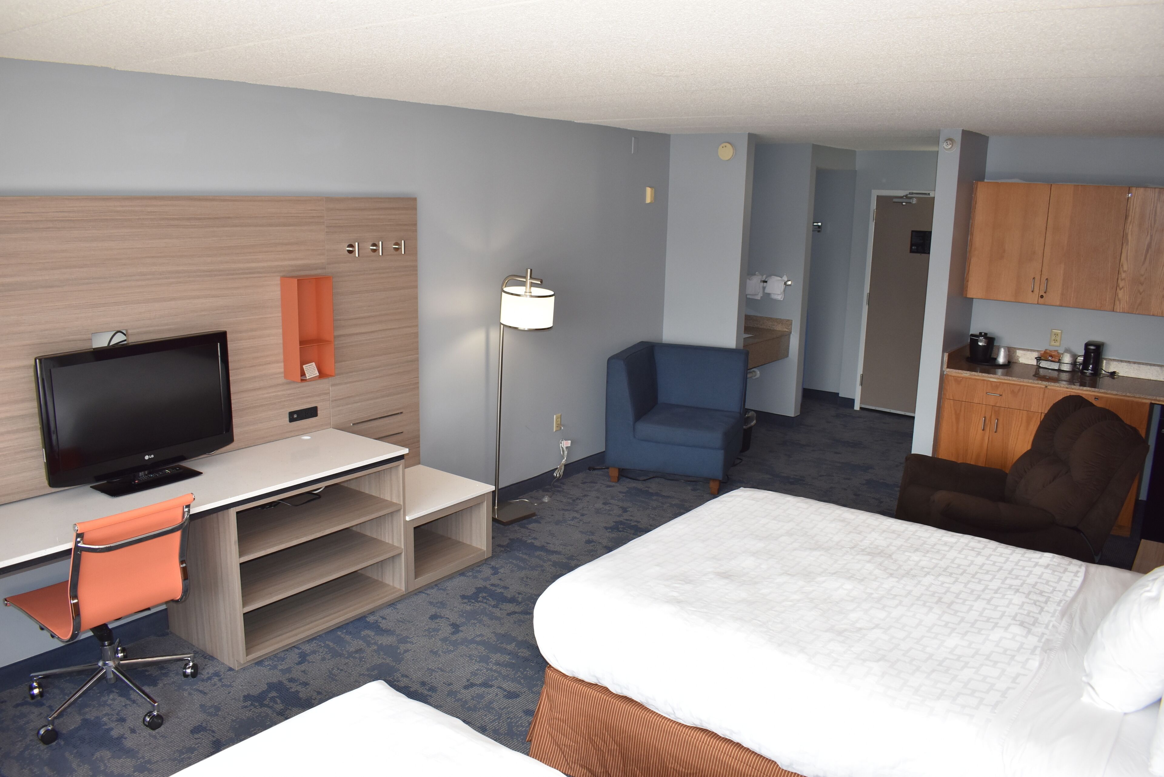 A hotel room with a bed, desk, television, chair, and kitchenette.